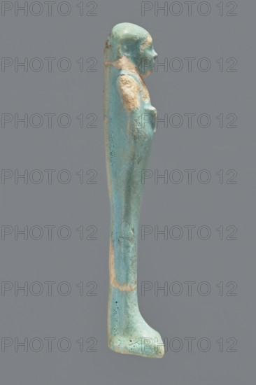 Ushabti, Mummy-shaped figurine. Standing on a base with a flat pillar at the back. Arms folded across the chest with delicately outlined hands visible from under the shroud. Both hands hold hoes, and a basket is slung over the left shoulder on the back. Wearing a smooth, tripartite wig. Round face with proportionate facial details. Not inscribed. 664–332 BC; Late Period, Egypt. Ushabti; height 11 cm., A slender upright figurine viewed in profile, with a smooth elongated form and a small rounded head, rendered in turquoise and light blue tones with patches of pale beige and hints of darker greenish-blue; the surface shows areas of wear and tiny pitted textures, and the figure has subtle raised contours suggesting arms and a slight facial profile, all set against a plain gray background.