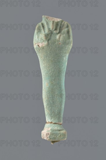 Shabti, mummy-shaped figurine, standing on a base; head missing. Narrow, slightly convex pillar at the back. Arms crossed high on the chest, right folded over left. Left hand holds a pickaxe, right a mattock, with a twisted rope passed over the left shoulder; a vertically hanging bag attached to the rope on the back. Convex tools; handles of both tools slightly curled at the ends. Smooth tripartite wig and short straight beard. Not inscribed. 664–332 BC, Late Period, Egypt. Height 11 cm., A single elongated object with a tapered cylindrical shape is shown against a plain gray background; the object has a weathered, rough surface in shades of turquoise and light blue with areas of pale beige where material is chipped away, a wider rounded top that shows shallow grooves and indented marks, a narrower midsection, and a slightly flared base that appears chipped and uneven with a small fragment protruding from beneath.