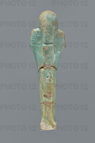 Ushabti, Mummy-shaped figurine shabti. Standing on a base with a flat pillar behind it. Arms folded across the chest with only the palms protruding from under the shroud. Hoe in the right hand and pickaxe in the left; ends of the handles slightly curled and tools rendered convex. A twisted rope slung over the left shoulder in the right hand, with a trapezoidal basket hanging from it on the back. Smooth three-part wig, long braided beard, round face with proportionate facial details. Not inscribed. Late Period, Egypt, 664–332 BC. Height 12.2 cm., A small elongated object shaped like a human figure, shown against a solid gray background, with a smooth rounded head and simplified arm shapes extending slightly from the sides; the surface is predominantly turquoise with areas of pale green, light blue, and patches of tan and brown discoloration, along with a few rough, worn spots and small chips revealing a lighter, off-white material at the base; the left arm area shows a textured grid pat...