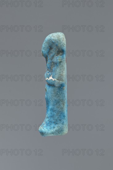 Ushabti, mummy-shaped figurine impressed in a mold, carelessly made of faience. The back is flat and unfinished. Arms crossed on the chest, right hand folded over the left; arms are distinct. Tools almost invisible — faint outline on the right shoulder of a tool or string for hanging a basket. Smooth three-part wig with front strands reaching the breasts toward the center of the chest; back strand not cut from the back. Ears exposed, large, vaguely modeled. Facial details illegible; false beard barely visible. Front of the legs shows irregularities and lines suggesting an inscription, now completely illegible. Figurine is cracked at waist level and glued together; glaze surface heavily worn., if there was an inscription, c. 1069–c. 715 BC; Third Intermediate Period, Egypt. Shabti; height 5.6 cm, width 2 cm, depth 1.7 cm., A vertical blue object with a rounded top and a slightly flared base suspended against a plain gray background, showing a textured surface with areas of lighter and d...