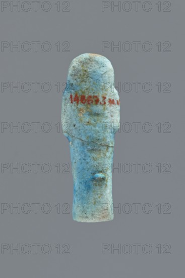 Ushabti, Mummy-shaped figurine, impressed in a mold, carelessly made of faience; back flat and unfinished. Arms crossed on the chest with right hand over left; arms distinct. Tools almost invisible — faint outline on the right shoulder of a tool or string for hanging a basket. Head with a smooth three-part wig, front strands reaching to the breasts toward the center of the chest; back strand not cut from the back. Ears exposed, large, vaguely modeled. Facial details illegible; false beard barely visible. Irregularities and lines on the front of the legs suggest an inscription, now completely illegible. Figurine cracked at waist and glued; glaze surface heavily worn. Typology Schneider: 4.5.4 4.5.2 ? VIIIA2/W17 H8 I0 Tp0 Tp7a ? if there was an inscription, c. 1069–c. 715 BC; Third Intermediate Period, Egypt. Shabti; height 5.6 cm, width 2 cm, depth 1.7 cm., A small, upright figurine-like object with a rounded top and a tapered base is shown against a plain gray background; the object is...