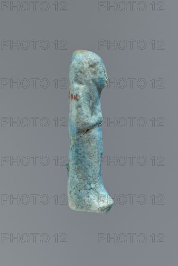 Ushabti, Mummy-shaped figurine, funerary offering, impressed in a mold, carelessly made of faience. The back of the figurine is flat and unfinished. Arms crossed on the chest, right hand folded over the left; arms distinct. Tools are almost invisible — on the right shoulder a faint outline of a tool or string for hanging a basket. Head wears a smooth three-part wig; front strands reach to the breasts toward the center of the chest, the back strand not cut from the back. Ears exposed, large, vaguely modeled. Facial details illegible. A false beard is barely visible. Front of the legs show irregularities and lines suggesting an inscription, now completely illegible. Figurine is cracked at the waist and glued together; the glaze surface is heavily worn., - if there was an inscription, c. 1069–c. 715 BC; Third Intermediate Period, Egypt; shabti; height 5.6 cm, width 2 cm, depth 1.7 cm., A vertically oriented, irregularly shaped object resembling a small sculpted figure is centered against ...