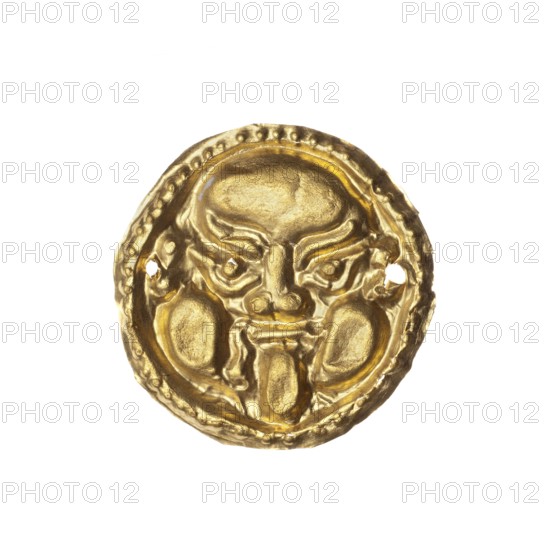 Appliqué in the shape of a Gorgon's head. Decorative appliqué for a tunic made of thin gold plate depicting the face of a Gorgon with its characteristic grimace – puffed out cheeks and protruding tongue. A large, round face with a low forehead, over which curled strands of serpentine hair fall. Large, oval eyes with marked pupils are set under strongly defined, arched eyebrows. The appliqué has four perforations on the edges used to attach it to a tunic. 5th–4th century BC, Greece, appliqué; height 2 cm, width 2.2 cm., A circular metallic object with a shiny gold color fills the center of the image, showing a raised three-dimensional face with prominent brow ridges, deep-set eyes, a broad nose, rounded cheek areas, and a tongue-like protrusion from the mouth; the outer rim has a beaded texture and irregular edges, and the object has small holes near the sides, all set against a white background.