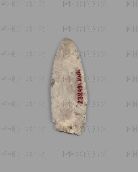 Javelin head, militaria; arrowhead/ranged weapon made of metal, Eastern Gaulish scenography style, 4th millennium BC; Southern Mesopotamia findspot, origin: Sumer; function: weapon; weight 10 g, A roughly elongated, pointed object with an irregular, chipped base rests against a plain gray background; the object is primarily off-white with subtle beige and light brown speckling, a few darker brown spots, and a narrow area of red along one side; its surface appears grainy and slightly rough.