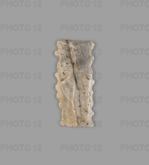 Blade — insert for a sickle; flint tool; Sumer; Uruk culture, ca. 4th–3rd millennium BC ca. 4000–3100 BC; Southern Mesopotamia; sickle tool., A vertically oriented, irregularly shaped stone fragment with scalloped edges shown against a uniform gray background; the stone displays a range of beige, tan, light brown, off-white, and gray tones with darker speckles and subtle streaks, a shallow central groove running lengthwise, and faint curved incised lines on one side, with a slightly rough, weathered surface texture.