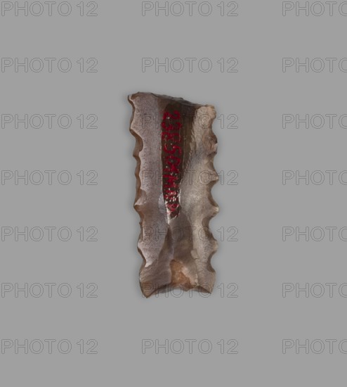 Blade - insert for a sickle, 4th–3rd millennium BC, Nippur, tool, A roughly rectangular, jagged-edged stoneflake with a flaked, sculpted surface sits against a flat gray background; the stone shows a palette of brown, tan, beige, and gray with areas of glossy sheen and matte texture, and there is a vertical streak of deep red on its surface.