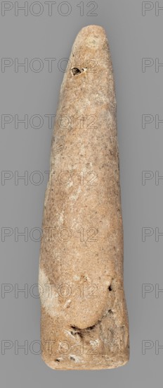 Mosaic cone, mosaic cones, decorative element, Uruk culture ca. 4000–ca. 3100 BC, Uruk Warka, Iraq, Sumer, 2nd half of 4th millennium BC, Southern Mesopotamia, Sumer, architectural decoration element, weight 44 g, A tall, elongated stone object with a smooth, tapered form displayed against a plain gray background; the stone shows a range of colors including light tan, sandy beige, warm brown, and patches of pale off-white, with several darker brown speckles and small rougher areas; its surface has subtle mottling and irregular textures, including a few small pits, shallow depressions, and rougher chips near the narrower end and along the wider base; overall the object appears rounded and slightly uneven in width with a natural, weathered appearance.