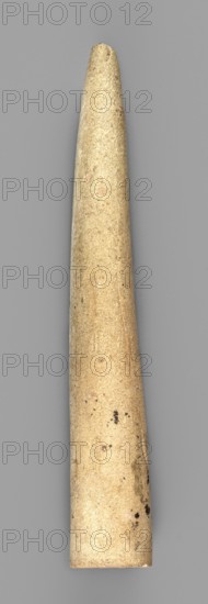 Mosaic cone, decorative elements, Uruk Culture ca. 4000–ca. 3100 BC, mosaic cones, Sumer, Uruk commonly known as Warka, Iraq, 2nd half of the 4th millennium BC, Sumer, Southern Mesopotamia, element of architectural decoration, diameter 1.2 cm, length 7.7 cm, A single elongated tapered cylindrical object with a rounded narrow end and a wider flat base, shown against a smooth neutral gray background; the object is a beige to light tan color with subtle variations in tone, small darker speckles and spots, minor surface imperfections, and areas of slightly darker discoloration near the wider end.