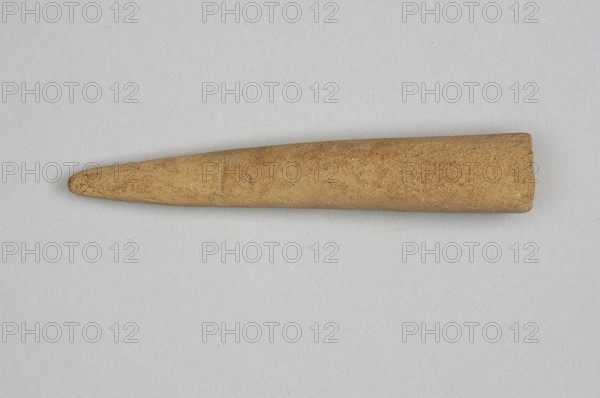 Mosaic cone, mosaic cones, ; decorative elements; Sumer; Near Eastern architecture; Eastern Gallic Scenography; 4th millennium BC; Uruk culture; Sumer type of site / place of origin; Southern Mesopotamia type of site / place of discovery; element of architectural decoration., A single elongated, tapered object rests horizontally against a light gray background; the object has a smooth, slightly textured surface in shades of tan and light brown with subtle speckling, appearing narrower and rounded at one end and broader and flatter at the other, with faint surface marks and a small indentation visible along its length.