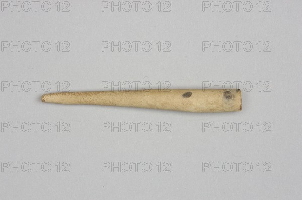 Mosaic cone, mosaic cones, decorative elements, Sumer, Near Eastern architecture, Eastern Gallic Scenography, 4th millennium BC; Uruk culture, Sumer, Southern Mesopotamia, element of architectural decoration, unknown creator/author., A single elongated tapered object lies horizontally against a neutral flat background, showing a cylindrical thicker end that narrows to a rounded tip; the object is mostly beige with areas of darker brown discoloration and small dark spots, and the background appears light gray.