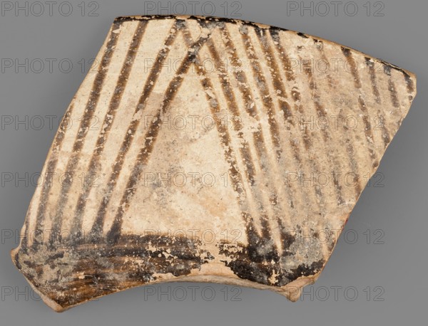 Fragment of a bowl, unknown Northern Mesopotamian workshop, painted pottery with geometric motifs, bowl fragment. Fragment of a bowl wall with a preserved thin rim edge and a transition to a flat, bottom. Before firing, the decoration consisting of geometric motifs was painted with ferrous clay on both sides of the bowl, over a layer of dry, very smoothed glaze. After firing, the painted decoration ranged in color from red to dark brown, while the background is shiny and cream-colored. The geometric motifs on the interior consist of groups of horizontal continuous and dotted lines, alternating with double lines, on which are placed small, elongated ovals. On the outer side, the decoration is a striped composition consisting of groups of several parallel diagonal lines inclined alternately to the left and to the right, and alternating triangular fields where the diagonal lines meet. Ca. 6500–ca. 5500 BC; Halaf culture, Northern Mesopotamia Iraq, Syria, Turkey. Pottery fragment; height 4...