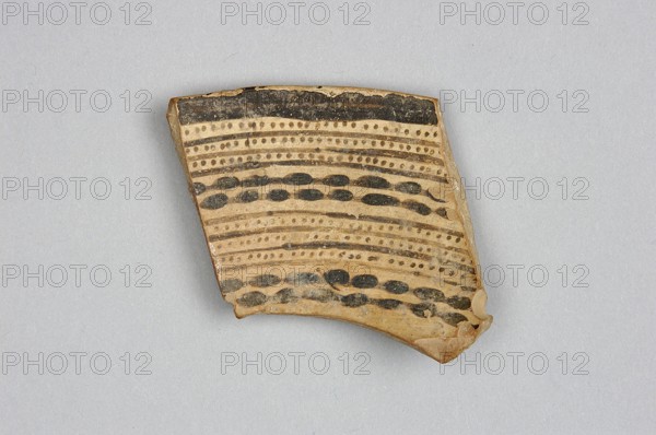 Fragment of a bowl, unknown Northern Mesopotamian workshop, painted pottery with geometric motifs, fragment of a bowl wall with a preserved thin rim edge and a transition to a flat, bottom. Before firing, the decoration consisting of geometric motifs was painted with ferrous clay on both sides of the bowl, over a layer of dry, very smoothed glaze. After firing, the painted decoration ranged in color from red to dark brown, while the background is shiny and cream-colored. The geometric motifs on the interior consist of groups of horizontal continuous and dotted lines, alternating with double lines, on which are placed small, elongated ovals. On the outer side, the decoration is a striped composition consisting of groups of several parallel diagonal lines inclined alternately to the left and to the right, and alternating triangular fields where the diagonal lines meet. Ca. 6500–ca. 5500 BC; Halaf culture, Northern Mesopotamia Iraq, Syria, Turkey. Pottery fragment; height 4.6 cm, width 5....