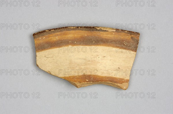 Fragment of a bowl, unknown northern Mesopotamian workshop; painted pottery with geometric ornaments; bucranium ornament; upper fragment of the bowl wall with preserved rim and geometric decoration painted on both sides. Outer side: two parallel red bands of different widths separated by an empty stripe on a cream-colored background. Inner side: in a band bounded by horizontal lines, two highly schematic, linearly stylized bucraniums bull heads with horns, arranged base to base. Narrow rim decorated with painted, irregularly rounded triangles with bases on the outer edge. Painted decoration applied before firing from carefully polished ferrous clay onto a dry, very smooth layer of glaze; after firing the paint ranges from red to dark brown, background glossy cream-colored. Ca. 6500–ca. 5500 BC; Halaf culture, Northern Mesopotamia Iraq/Syria/Turkey; pottery fragment; weight 16 g., A broken pottery sherd with a curved rim is shown on a light gray background; the sherd displays a banded s...