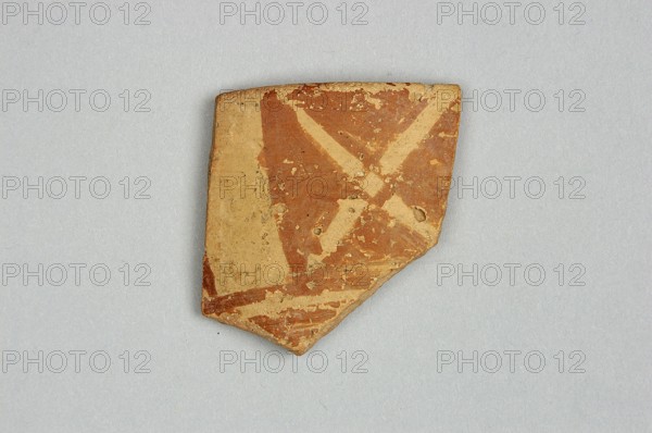 Fragment of a bowl spout, 6th millennium BC, Northern Mesopotamia, vessel, A broken piece of pottery with a triangular outline sits on a light gray background, showing a surface of reddish-brown and beige with chipped and worn areas, a few rough edges, and patches of lighter beige where the top layer has flaked away.