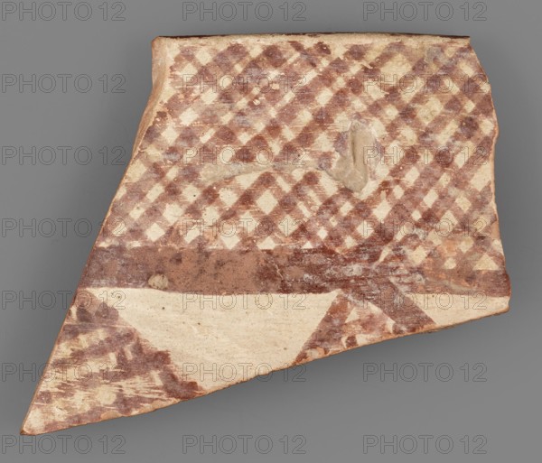 Fragment of a bowl, unknown Northern Mesopotamian workshop, painted pottery, geometric motifs, bowls. Fragment of the wall of a bowl or cup with a preserved pointed rim. On the outside, the decorative composition consists of from the top: a wide band of diagonally intersecting parallel lines, terminated at the bottom by a thick line. Below is a fragment of another band filled with a row of triangles or rhombuses filled with diagonally intersecting lines. On the inside, the decoration is limited only to the upper part of the vessel and consists of a wide band terminating at the bottom with a wavy line. c. 6500–c. 5500 BC; Halaf culture ca. 5200–ca. 4500 BC earlier date. Northern Mesopotamia Iraq/Syria/Turkey. Pottery fragment; height 3.8 cm, width 3.8 cm, depth 0.48 cm, weight 8 g., A broken, flat fragment of pottery with a checkered painted pattern in reddish-brown and off-white, showing a large triangular shape and irregular edges; the surface has worn areas and a small rounded depres...