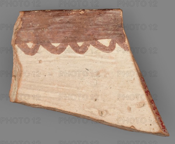 Fragment of a bowl, unknown Northern Mesopotamian workshop, painted pottery with geometric motifs, bowls, Eastern Gaulish Scenery. Fragment of the wall of a bowl or cup with a preserved pointed rim. On the outside, the decorative composition consists of from the top: a wide band of diagonally intersecting parallel lines, terminated at the bottom by a thick line. Below is a fragment of another band filled with a row of triangles or rhombuses filled with diagonally intersecting lines. On the inside, the decoration is limited only to the upper part of the vessel and consists of a wide band terminating at the bottom with a wavy line. c. 6500–c. 5500 BC; Halaf culture ca. 5200–ca. 4500 BC, Northern Mesopotamia Iraq/Syria/Turkey. Pottery fragment; height 3.8 cm, width 3.8 cm, depth 0.48 cm, weight 8 g., A fragment of a flat, triangular ceramic shard with a smooth, pale beige surface and a rougher, darker brown top edge that features a scalloped painted pattern; the shard shows worn, uneven e...