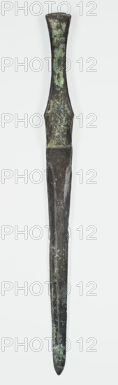 Short sword, unknown Luristan workshop. A short sword with a cast blade and a mushroom-shaped hilt with a rimmed mount, the raised edges of which served to hold the lost hilt casing. The casing may have been made of bone, wood, horn, or stone. In the lower part of the casing, two low, crescent-shaped protrusions of sheet metal are bent inward to secure the casing. The hilt flows directly into a double-edged blade with a centric point. Behind the short, rectangular, double-blunt base, the blade tapers evenly towards the tip. A slightly convex ridge runs through the center of the blade, which splits towards the base in its upper part. Iron Age, 9th–6th century BC Iron Period II; Iran, Luristan. Weapon. Height 40.6 cm; width 3.4 cm; depth 2 cm; weight 208 g., A long metal object with a narrow pointed end and a wider handle, shown vertically against a light background, with a surface that is dark brown to black and mottled with patches of green and pale green corrosion; the handle is sligh...