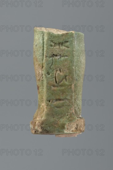 Shabti legs, mummy-shaped figurine fragment knees down. Feet rest on a base with a flat pillar at the back. Inscription preserved in fragments, placed in a column on the front of the legs and on the pillar. Late Period, Egypt, 664–332 BC. Shabti; height 4.2 cm., A roughly cylindrical fragment with an uneven top edge showing a worn interior surface, the exterior coated in a green glaze with areas of muted brown and beige where the glaze has chipped or worn away, a few shallow incised marks and small pits on the glazed surface, and a small rounded base portion with rough beige and brown exposed material, all set against a plain gray background.