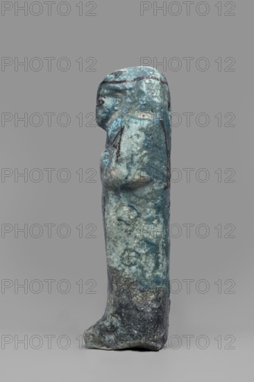 Ushabti of Amenmose, Mummy-shaped funerary figurine shabti, c. 1069–c. 656 BC, Third Intermediate Period, Egypt. Height 16.4 cm, width 5.3 cm. Arms crossed on the chest, right arm folded over left; holds hoes in both hands; a basket on the back. Smooth tripartite wig with headband, ears uncovered; large eyes; mouth and nose not distinct. Tools, facial details, and headband painted with dark paint. Painted inscription in a framed column: Osiris the prophet of Amun Amenmose, justified by the voice., A small standing statuette shown in profile against a plain gray background, with a weathered surface that is predominantly turquoise and blue with areas of greenish patina and darker gray to black patches, showing a rounded head, a simplified facial profile, a wrapped or draped body with an arm held across the front, and a broad base or foot at the bottom; the surface is pitted and mottled with lighter and darker spots and streaks.