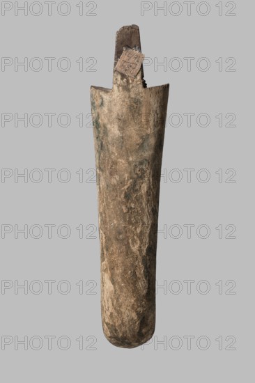 Beard from a sarcophagus mask, slightly curled; sarcophagus fragments; beards facial hair; masks., Sarcophagus mask, ca. 1550–332 BC New Kingdom–Late Period, Egypt. Height 16.2 cm., A tall, narrow cylindrical wooden object with a rounded bottom and a slightly flared top, showing a rough, weathered surface in shades of brown with patches of darker brown and hints of green; the top has a broken, jagged wooden piece protruding with a small square of coarse woven material attached, the woven patch appearing tan and brown; the background is a uniform light gray.