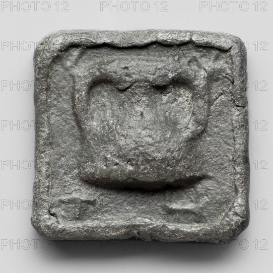 Lead weight, repossession Frombork; Warmian-Masurian Voivodeship, Greek letters in the corners EMIT; Athens, Attica, 4th–2nd century BC; weight; height 3.9 cm, width 3.9 cm, depth 0.8 cm, weight 158.3 g, A square, slightly irregular metal object with a rough, textured surface in shades of gray and silver, featuring a raised central area with a rounded, heart-like indentation and a recessed border around the edges; the metal shows uneven patina with darker gray crevices and lighter silver highlights, and the background is a smooth, pale gray.