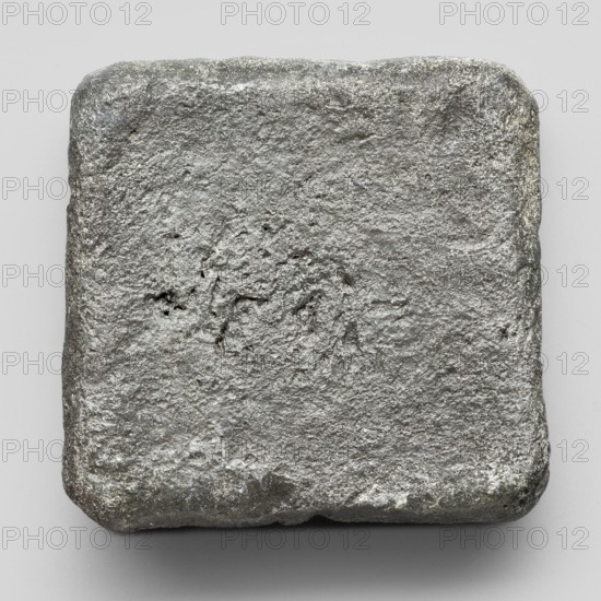 Lead weight, Greek letters in the corners EMIT; Athens, Attica; 4th–2nd century BC; weight; height 3.9 cm, width 3.9 cm, depth 0.8 cm; weight 158.3 g., A roughly square, slightly rounded object with a coarse, uneven surface in shades of gray and silver sits against a light gray background; the object shows a textured, metallic appearance with darker gray areas and lighter silvery highlights across its top and edges, and a few small pits and irregularities on its surface.