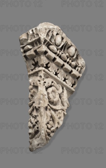 Fragment of architectural decoration. Corner section of a fragment made in relief. The cornice is decorated with bands of ovoids, pearls, cubes, and acanthus leaves. The band decoration is separated by a thin roller from part of the frieze, which depicts a plant tendril with a rosette and a bird. Deep, plastic relief, background drilled. 1st–2nd century, Italy. Roman architecture; cymatium; friezes; bird and plant decorative motifs; bas-relief. Height 45 cm, width 30 cm, depth 15 cm maximum, depth 7 cm minimum, weight 15.354 kg., A carved stone fragment with intricate raised reliefs showing floral and leaf motifs and rounded bead-like forms, displayed against a flat gray background; the stone appears weathered with a surface texture of pitting and erosion, and its colors range from light beige to warm gray with small areas of darker gray and subtle off-white patches.