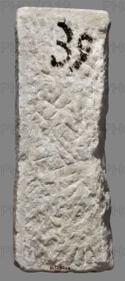 Fragment of a sarcophagus, unknown Roman workshop, end of the 3rd century, Roman Empire 27 BC–476, sarcophagus; height 47 cm, width 16.5 cm, depth 9 cm, weight 15 kg., A vertical rectangular stone slab with a rough, pitted surface in shades of white and off-white set against a plain gray background; there is a patch of dark, almost black irregular markings near the top and a small area of darker brownish discoloration near the bottom edge.