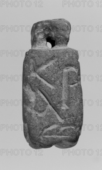 Limestone Christian amulet in the shape of an elongated hexagon with Greek inscription. Text in Greek on the sides and on the bottom; letters on five edges form a coherent inscription with magical meaning. Protrusion with a drilled hole on the upper edge, likely used to attach a strap or chain. Date: 2nd–3rd century . Place of finding: Miletus. Function: amulet. Dimensions: height 5.2 cm, width 2.3 cm. Maker/creator: unknown., A roughly rectangular stone object with a textured, weathered surface and a small rounded hole near the top, showing carved shallow grooves and raised ridges on its face; the stone appears in shades of gray with darker and lighter gray variations across its uneven surface, set against a pale gray background.