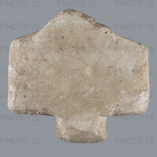 Greek dedicatory inscription, Horus myth., tombstones, inscriptions, Late Roman Empire period, Egypt, Greek inscription; height 12.1 cm, width 13.4 cm, depth 1.2 cm, A roughly rectangular stone object with a trapezoidal top edge and a small protrusion at the bottom, showing an uneven, weathered surface. The stone displays a range of beige and off-white tones with areas of light brown and pale gray, along with small darker brown specks and faint whitish patches. The edges are worn and slightly rounded, with subtle surface scratches and pitting visible across the face. The background behind the stone is a uniform mid-gray color.