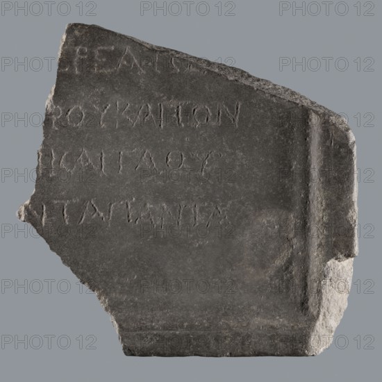 Fragment of a Greek dedicatory inscription, unknown author, tombstone inscription, 70 BC–1 AD; end of the Ptolemaic period or beginning of the Roman period, Egypt, Greek inscription, height 24.2 cm, width 24 cm, depth 4.7 cm, A broken dark gray stone fragment with a rough uneven edge on one side and a more squared, chipped edge on the opposite side, showing a slightly recessed rectangular panel and shallow incised marks across its face; the surface varies in tone from dark gray to lighter gray at the chipped areas, with subtle texture and weathering visible.