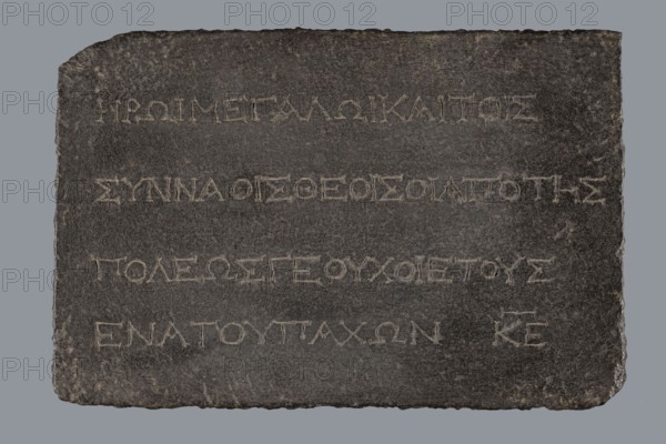 Greek dedicatory inscription, unknown author, tombstone inscription, 2nd half of the 2nd century BC, Egypt; Greek inscription; height 22.0 cm, width 32.5 cm, depth 7.0 cm, A dark rectangular stone slab with rough uneven edges resting against a plain neutral background, showing a textured surface with chiseled grooves forming horizontal rows; the slab is primarily dark gray with lighter gray scratches and worn areas, and the carved grooves appear as lighter gray lines that contrast with the darker surface, while the edges show some brownish and slightly lighter gray weathering.