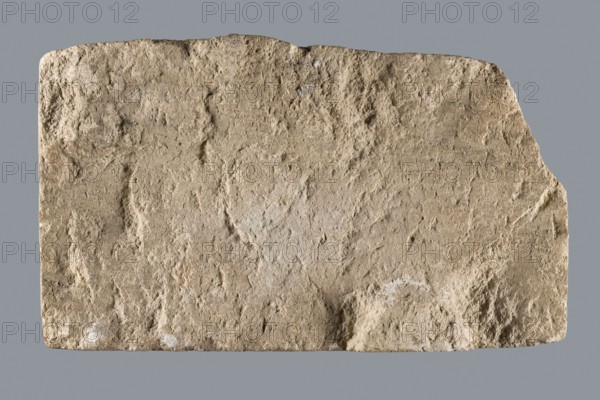 Slab with a Latin votive inscription for Fortuna Conservatrix, Caius Iulius Maianus, 2nd–3rd century; limestone slab with smoothed front surface and sides and an irregular back, upper left corner missing. Front bears a carved inscription in five lines; letters were at some point painted red two paint types: darker in most letters and a lighter, very thick paint in the letter E in line 2. Associated with Fortuna mythology, Latin inscriptions, baths, centurions, Germania Superior, Roman legions. Votive slab, width 33 cm, height 18 cm, thickness 6 cm; found at Bad Ems presumably in the baths of the Roman fort., A roughly rectangular, weathered stone slab with an uneven, pitted surface and irregular edges sits against a flat background. The stone displays a range of beige and tan tones with areas of light brown, pale cream, and faint grayish patches. The surface texture is coarse and granular, showing depressions, raised ridges, and small rough nodules. The top edge is slightly jagged and ...