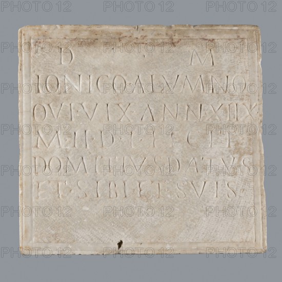 Latin grave inscription, unknown author, 2nd century, Roman Empire 27 BC–476, slab epitaph, grave inscription, height 31 cm, width 28 cm, A square pale beige stone plaque with a slightly raised border sits against a neutral gray background. The plaque surface shows a weathered, uneven texture with small chips and areas of darker beige and faint brown discoloration. There is a shallow rectangular recessed area within the border, and shallow carved grooves and lines are visible across the surface. The stone has lighter cream highlights and subtle off-white areas, and a small darker spot appears near the bottom edge. Overall the visible colors include beige, cream, off-white, gray, and faint brown.