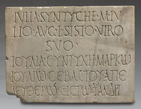 Tombstone of Marcus Julius Sistus with bilingual inscription, unknown Roman workshop, sepulchral funerary architecture, Greek inscriptions, Latin inscriptions, imperial freedmen. Rectangular marble slab with very irregularly worked back surface; front bears traces of numerous auxiliary lines vertical and horizontal into which three lines of Latin text and three lines of Greek text are rather unevenly inscribed. Date: after 14 AD–end of 1st century 1st century. Place of origin: Italy, possibly Rome. Slab: height 42 cm, width 56 cm, depth 5 cm, weight 29 kg., A rectangular stone slab with carved grooves forming rows of shapes, showing a pale off-white to light beige surface with areas of darker beige and small brown discolorations, and a few faint gray marks and hairline cracks; the slab has slightly rounded top corners, a chipped lower left corner, and a small triangular nick at the lower right edge; the carved lines create recessed letterlike forms in a regular, evenly spaced arrangeme...