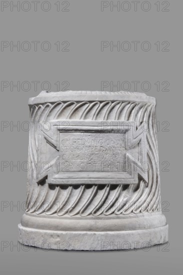 Urn of Gnaeus Pedanius Callistus with Latin inscription, unknown Roman workshop. A cylindrical funerary urn placed on a smooth plinth and a convex base. Its shape and decoration resemble a fragment of a column shaft, tapering towards the top. Entire surface decorated with S-shaped fluting strigillea, closed at top and bottom by a narrow frame. In the central part, slightly closer to the cornice than the base, is a tabula ansata with open handles containing the inscription. Inside the urn, a deep niche for ashes was chiseled out. The opening is topped by a molding decorated with radially arranged grooves; the place where the lid was attached is visible. Lid: missing; comparable examples have a conical or possibly domed roof. Inscription letter height 15 cm. Dating: beginning of the 3rd century previously dated late 2nd–3rd century AD. Probable findspot: Rome; place of origin: Roman Empire 27 BC–476. Urn Roman, weight 121.5 kg., A cylindrical stone object with carved spiral fluting aroun...