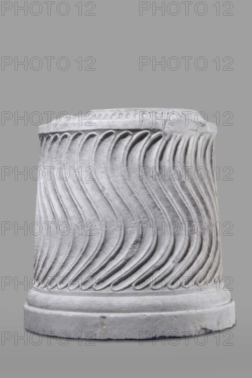 Urn of Gnaeus Pedanius Callistus with Latin inscription, unknown Roman workshop. A cylindrical urn placed on a smooth plinth and a convex base. Its shape and decoration resemble a fragment of a column shaft, tapering towards the top. Entire surface decorated with S-shaped fluting strigillea, closed at top and bottom by a narrow frame. In the central part, slightly closer to the cornice than the base, is a tabula ansata with open handles containing the inscription. Inside the urn a deep niche for ashes was carved out with a chisel. The opening is topped by a molding decorated with radially arranged grooves. The place where the lid was attached is visible. Lid: missing; a comparable urn has survived with its original conical lid, so it is assumed this urn likely had a similar conical or possibly domed lid. Inscription: letter height 15 cm. Dating: beginning of the 3rd century previously dated late 2nd–3rd century AD. Probable findplace: Rome; origin: Roman Empire 27 BC–476. Type: Roman u...