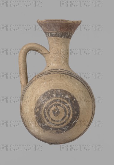 Cypriot gourd jug, Excavations at Nea Paphos Cyprus. Cypriot pottery, Cypriot Bichrome Ware III. Small vessel with a barrel-shaped gourd-shaped body, without a foot, with a spherical bottom. On both shorter sides the center is marked with a small protruding point. A single ring-shaped handle on the longer side, mounted above half the height of the body and at the base of the neck, curved downwards. Quite long neck, strongly flaring, conical spout. Yellow clay with yellow-brownish engobe. Decoration in black-brown and matte red: the spout externally has a wide matte red band beneath a narrower black band; the belly on both sides has two groups of three concentric black-and-brown lines of varying widths and spacing, with the outer line in the groups on the shorter sides much wider than the others. Protruding points are marked in black-and-brown. Date: 850–700 BC. Cyprus, vessel., A rounded ceramic vessel with a single curved handle and a flared neck is centered against a plain light gray...