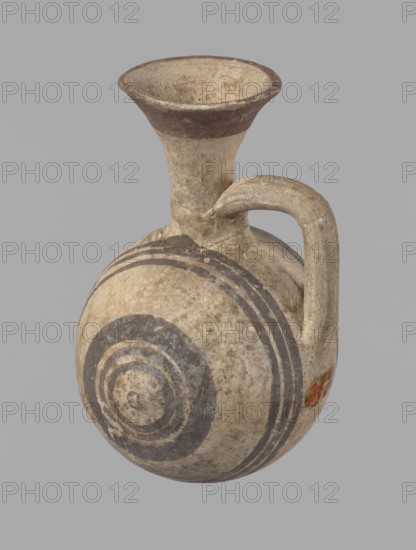 Cypriot gourd jug, Cypriot pottery, Cypriot Bichrome Ware III. A small vessel with a barrel-shaped gourd-shaped body, without a foot, with a spherical bottom. The center is marked with a small protruding point on both short sides. A single handle on the long side, mounted at the greatest bulge of the body and at the base of the neck, bent at a right angle. Quite long neck, strongly flaring, conical spout. Neck and handle slightly offset from the vessel axis; the handle is mounted at a slight angle, with a very clear trace of finger pressure on the right side where it is attached to the neck. Reddish-brown clay. Yellowish-brown engobe. Decoration in black-brown and matte red. The rim is decorated externally with a wide matte red band. The body is decorated on both sides with two groups of three concentric black-brown lines, of varying widths and spacing. In the groups on the shorter sides, the outer line is much wider than the others. Protruding points are marked in black-brown. Preserv...