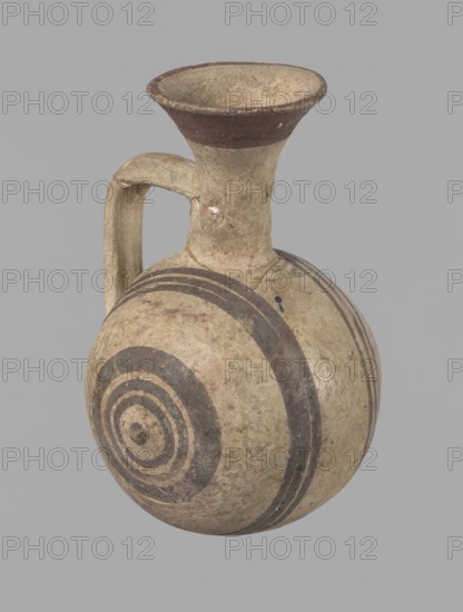 Cypriot gourd jug. A small vessel with a barrel-shaped gourd-shaped body, without a foot, with a spherical bottom. The center is marked with a small protruding point on both short sides. A single handle on the long side, mounted at the greatest bulge of the body and at the base of the neck, bent at a right angle. Quite long neck, strongly flaring, conical spout. Neck and handle slightly offset from the vessel axis; the handle is mounted at a slight angle, with a very clear trace of finger pressure on the right side where it is attached to the neck. Reddish-brown clay. Yellowish-brown engobe. Decoration in black-brown and matte red. The rim is decorated externally with a wide matte red band. The body is decorated on both sides with two groups of three concentric black-brown lines, of varying widths and spacing. In the groups on the shorter sides, the outer line is much wider than the others. Protruding points are marked in black-brown. Preservation condition: cracked and glued neck and ...