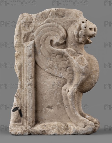 Bench support with a griffin figure, unknown Roman workshop, furniture, griffins myth., Roman sculpture, table or bench support decorated with a winged lion, ca. mid-1st century, Roman Empire 27 BC–476, furniture, sculpture; height 46 cm, width 32 cm, depth 9 cm, weight 19.7 kg, A carved stone relief shows a stylized winged creature in profile against a flat background. The creature has a rounded head with an open mouth and carved facial details, a curled decorative wing with scalloped feather patterns, a rounded body, and front legs ending in paws resting on a base. The stone surface displays weathering and rough texture with chips and worn edges. Visible colors include beige and light tan on the stone, small areas of darker gray and brown discoloration, a few spots of black, and a neutral gray backdrop.