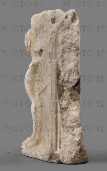 Bench support with a griffin figure; unknown Roman workshop; furniture; griffins myth.; Roman sculpture; table or bench support decorated with a winged lion; ca. mid-1st century; Roman Empire 27 BC–476; sculpture; height 46 cm, width 32 cm, depth 9 cm, weight 19.7 kg, A roughly vertical stone object with an irregular, weathered surface showing a mix of light beige, off-white, and pale tan tones, set against a smooth medium gray background; the stone has rounded and chipped edges, textured pitted areas, and smoother carved sections along one side that suggest a raised vertical ridge and a curved form resembling a partial limb or rounded feature, with subtle variations of darker beige and faint brownish spots in crevices and along the base.