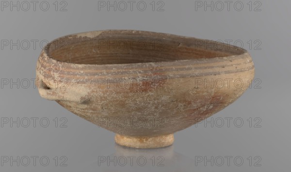 Bowl, excavations at Nea Paphos Cyprus - equivalent, vessels, Cypriot pottery, Bronze Age ceramics, footed bowl/goblet on a low ring-shaped stem; walls diverge at a strongly obtuse angle, bending slightly inward at three-quarters height with one small horizontal vise at the bend. Light-sand clay covered with light-brown paint on the outside and brown-red on the inside. Painted decoration on the outside: narrow horizontal lines slightly darker than the ground, two horizontal purple stripes under the rim; a stripe covering the edge of the rim; belly just below the rim. Inside: numerous light purple horizontal lines. 1650–1200 BC, Cyprus, vessel goblet, height 8 cm, width 17 cm, A shallow rounded bowl with a small foot, showing a weathered surface and textured patches, with a small applied handle-like protrusion on one side; the interior and exterior surfaces display concentric ridges near the rim and worn horizontal striations. The visible colors include shades of beige, tan, light brown...