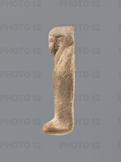 Shabti, Mummy-shaped figurine, standing on a base, the back supported by a flat pillar. Arms crossed on the chest, holding hoes in both hands. In the right hand a string from which a basket is slung over the left shoulder. Slightly convex tools. Smooth, tripartite wig. Round face with clearly defined large eyes; mouth and nose not visible. Not inscribed. 525–343 BC; Late Period, 27th–30th Dynasty, Egypt. Shabti; height 7 cm., A worn carved figure shown in profile with a rounded head and a simplified facial profile, a sloped shoulder and an elongated, straight torso that tapers down to a rounded foot-like base; the surface appears textured and pitted. The visible colors are shades of brown, tan, beige, and hints of pale yellow, set against a neutral gray background.