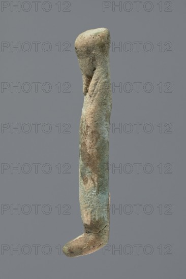 Ushabti, Mummy-shaped figurine, very schematically shaped. Hands crossed on the chest. On the head is a long, tripartite wig. Facial details illegible. Not inscribed. ca. 1069–ca. 656 BC; Third Intermediate Period, Egypt. Ushabti; height 9.4 cm., A single elongated vertical object with an irregular rounded top and a curved hooked end, showing a rough, pitted surface texture and small surface indentations; the object displays a mix of green, bluish, brown, beige, and gray tones across its surface, with patches of darker brown and lighter beige creating a mottled appearance, and it is set against a uniform gray background.