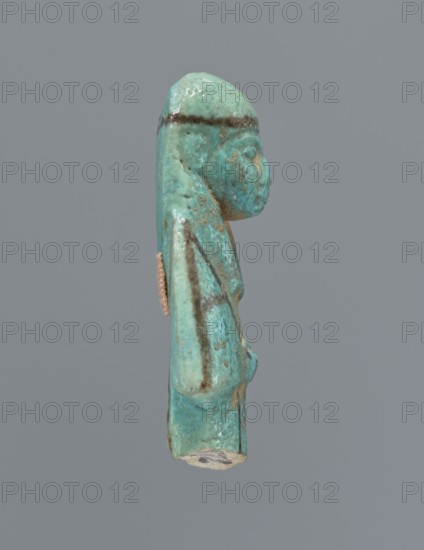 Ushabti, mummy-shaped figurine, preserved upper fragment from the waist up. Arms crossed on the chest, hands placed at the same level, next to each other, holding hoes in both hands. Rectangular basket on the back. Head wears a long, smooth, three-part wig with a headband. Triangular face with proportional details; eyes slightly closed. Headband and facial details painted. Painted inscription placed in a column separated by vertical lines on the front of the legs, starting just below the folded hands; text illegible. c. 945–c. 715 BC, Third Intermediate Period, 22nd–23rd Dynasty, Egypt. Height 5.8 cm., A small turquoise-green figurine viewed in profile against a plain gray background, showing a human-like head with a rounded top and a pronounced nose, a long headdress or hair that extends down the back, and a slightly protruding torso with an arm folded against the body; the surface shows areas of darker green and brownish streaks and spots, along with patches of lighter green and some...