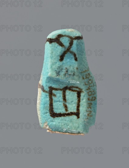 Ushabti, mummy-shaped figurine, preserved head and fragment of torso. Arms crossed on the chest, hands placed at the same level, next to each other, holding hoes in each hand. On the back, a square basket is slung on strings over both shoulders. On the head is a long, smooth, tripartite wig with a headband. Triangular face, details almost illegible. Headband and tools painted. ca. 945–ca. 715 BC; Third Intermediate Period, 22nd–23rd Dynasty, Egypt; height 3.7 cm, A small object with a turquoise blue surface suspended against a gray background, showing a few dark brown markings on its upper and middle areas and a darker brown outline forming a rough rectangular shape on its lower half, with some pale beige material visible along its bottom edge and a few tiny darker speckles across its surface.