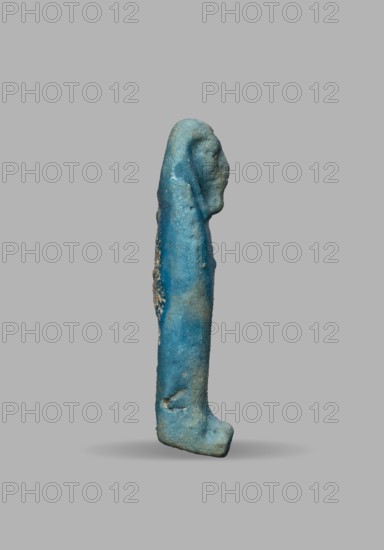 Ushabti, Wigs, funerary figurine, mummy-shaped figurine. The arms are not distinct, with a slight convexity of the clenched hands. Delicate outline of tools on the arms. On the head is a smooth, tripartite wig. The face is large and round with large eyes, a wide nose, and a slightly grimacing mouth. Not inscribed. 525–332 BC; Late Period, 27th–30th Dynasty, Egypt. Ushabti. Height 5.1 cm; width 1.5 cm., A vertical, elongated small statue or figurine shown in profile with a stylized human head and a long body ending in a short base, rendered in shades of blue with areas of lighter turquoise and some pale beige or sandy discoloration, with a rough, weathered surface texture and small granular encrustations on one side, set against a plain light gray background with a faint shadow beneath.
