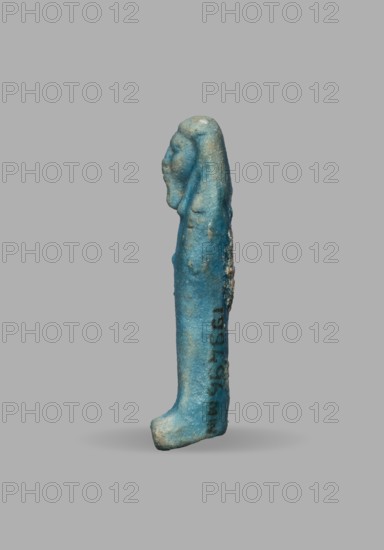 Ushabti, Mummy-shaped funerary figurine, wig, funerary figurine, grave good. The arms are not distinct, with a slight convexity of the clenched hands; delicate outline of tools on the arms. On the head is a smooth, tripartite wig. The face is large and round with large eyes, a wide nose, and a slightly grimacing mouth. Not inscribed. Date: 525–332 BC Late Period, 27th–30th Dynasty, Egypt. Dimensions: height 5.1 cm; width 1.5 cm., A small turquoise-blue elongated figurine stands upright against a plain gray background, showing the profile of a stylized human head with a rounded skull and a suggestion of facial features; the body tapers down to a slightly curved foot-like base, with areas of lighter bluish-green and small patches of pale beige wear or deposits along the surface, and a few darker bluish spots and subtle rough textures visible on the side.