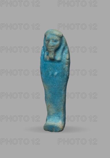 Ushabti, Wigs, funerary figurine, mummy-shaped figurine. The arms are not distinct, with a slight convexity of the clenched hands. Delicate outline of tools on the arms. On the head is a smooth, tripartite wig. The face is large, round, with large eyes, a wide nose, and a slightly grimacing mouth. Not inscribed. 525–332 BC; Late Period, 27th–30th Dynasty, Egypt. Ushabti; height 5.1 cm, width 1.5 cm., A small sculpted figure shown against a plain gray background, rendered in bright turquoise blue with areas of lighter blue and some pale beige discoloration; the figure has a rounded head with a suggestion of facial features and a headdress-like form extending down the sides, a narrow elongated body tapering toward a slightly thicker base, a textured surface with small pits and worn spots, and soft shadow beneath it.